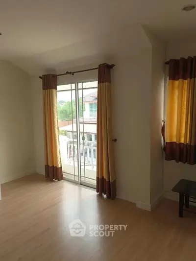 Spacious room with large windows and balcony access, featuring elegant curtains and wooden flooring.