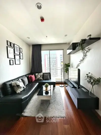 Modern living room with sleek black sofa, wall-mounted TV, and balcony view.