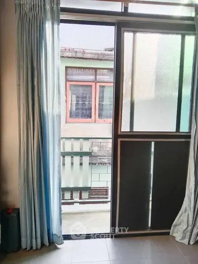Cozy apartment balcony with sliding glass door and curtains, offering urban view.