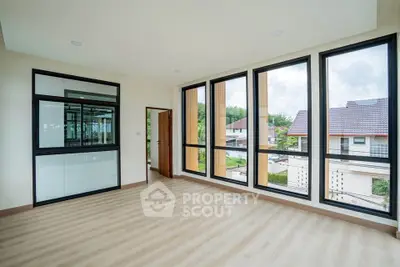 Spacious modern room with large windows and wooden flooring, offering a bright and airy atmosphere.