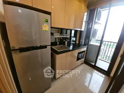 Modern kitchen with sleek cabinets, stainless steel fridge, and balcony view.