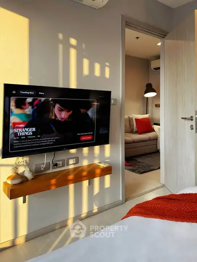 Modern bedroom with wall-mounted TV and cozy living area in view, featuring stylish decor and natural lighting.