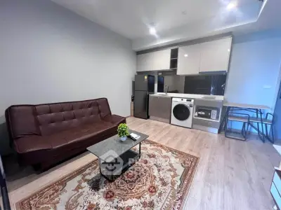 Modern living room with open kitchen, featuring a brown sofa, stylish rug, and sleek appliances.