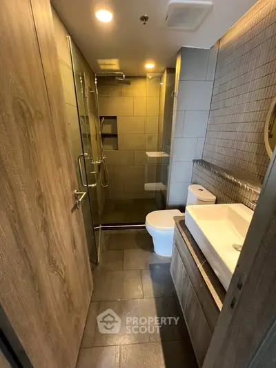 Modern bathroom with sleek design, featuring a glass shower, wooden accents, and contemporary fixtures.