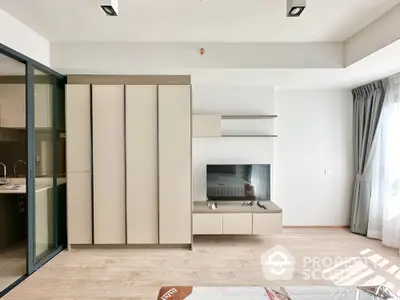 Modern bedroom with sleek wardrobe and TV unit, natural light streaming through large window.