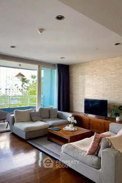 Spacious living room with modern decor and large windows opening to a balcony with city view.