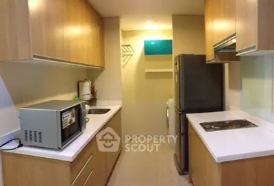 Modern kitchen with wooden cabinets, microwave, and sleek countertops in a cozy apartment.