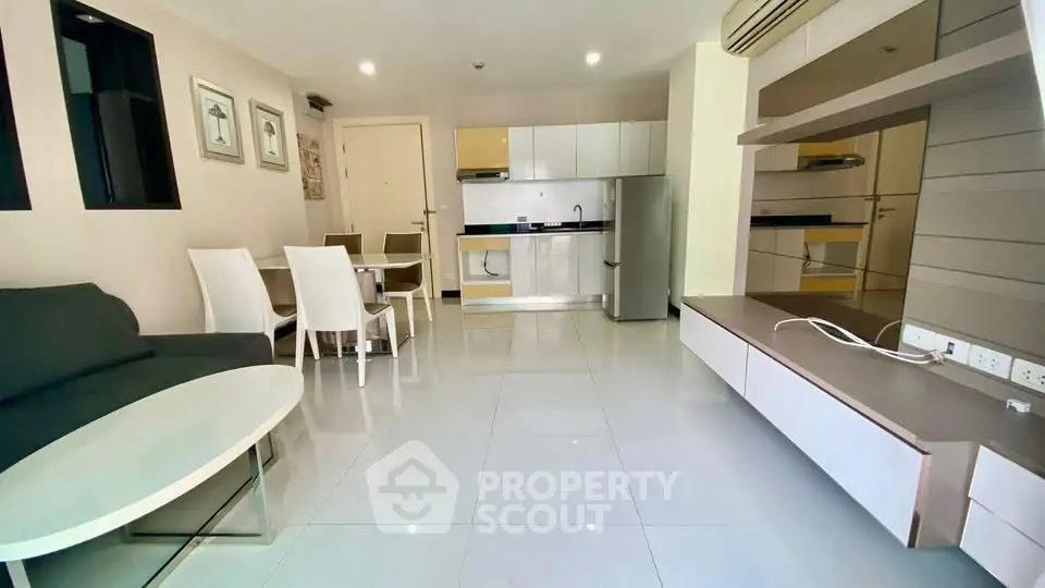 Modern open-plan living room with sleek kitchen and dining area, featuring glossy tiles and contemporary furniture.