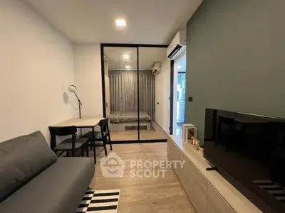 Modern living room with sleek furniture and glass partition leading to bedroom.