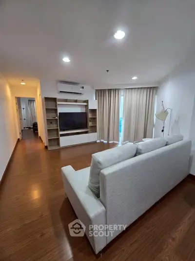 Spacious living room with modern decor and natural light, featuring a cozy sofa and entertainment center.
