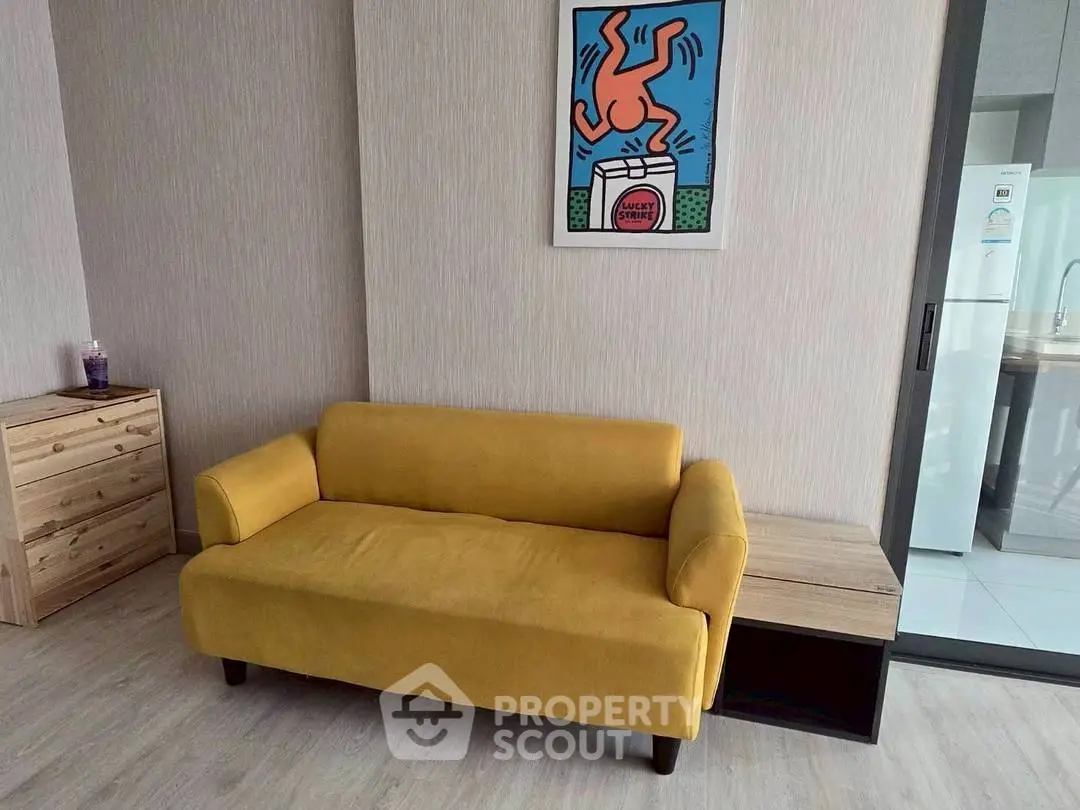 Modern living room with vibrant yellow sofa and stylish wall art, adjacent to a sleek kitchen area.
