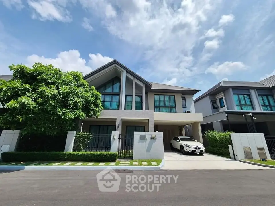 Modern two-story house with driveway and car, featuring sleek architecture and lush greenery.