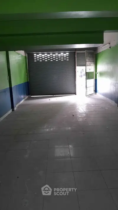 Spacious commercial space with tiled flooring and roll-up shutter, ideal for retail or storage.