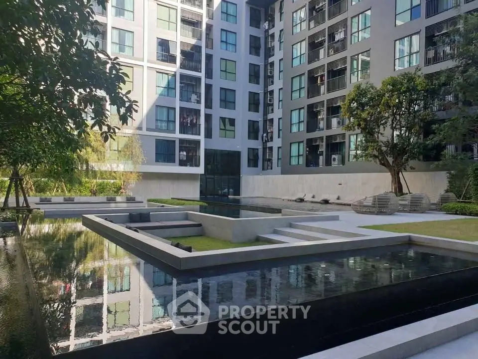 Modern apartment building with serene water feature and lush greenery in courtyard.