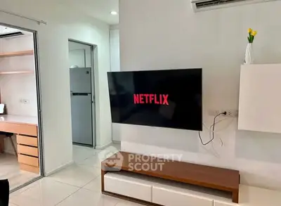 Modern living room with wall-mounted TV and sleek furniture, adjacent to a study area and kitchen.