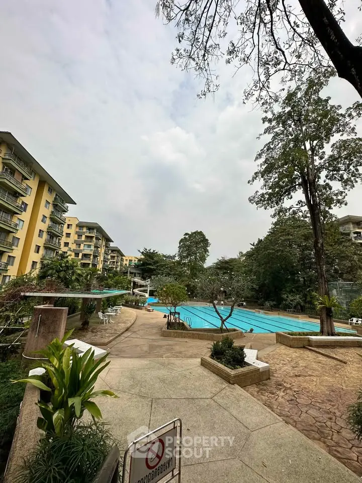 Spacious outdoor pool area in a residential complex with lush greenery.