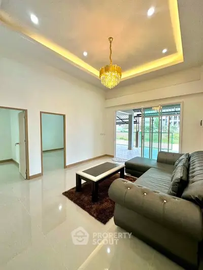 Spacious living room with elegant chandelier and modern sofa, featuring large windows for natural light.