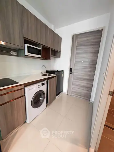 Modern compact kitchen with washing machine and microwave in sleek apartment.