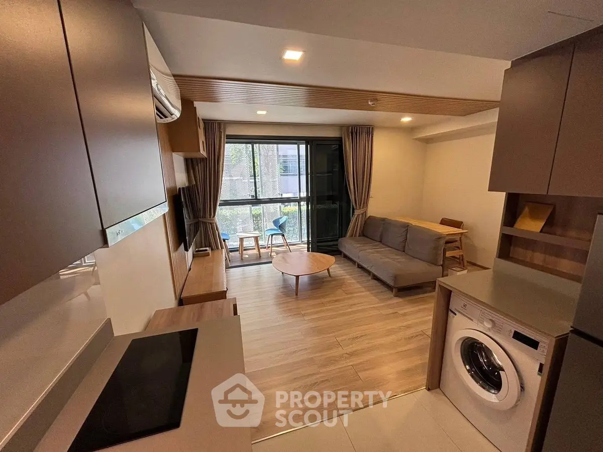 Modern living room with open kitchen and washing machine, featuring a cozy balcony view.