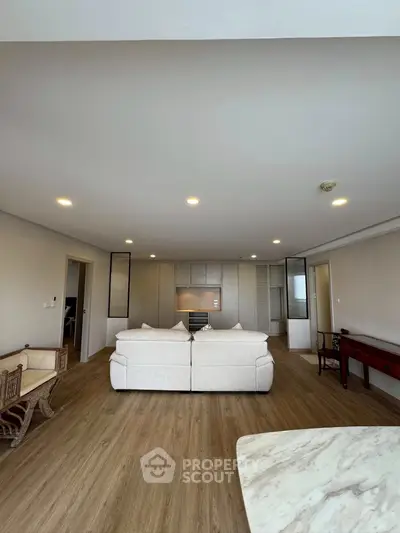 Spacious modern living room with elegant wooden flooring and cozy white sofas, perfect for relaxation.