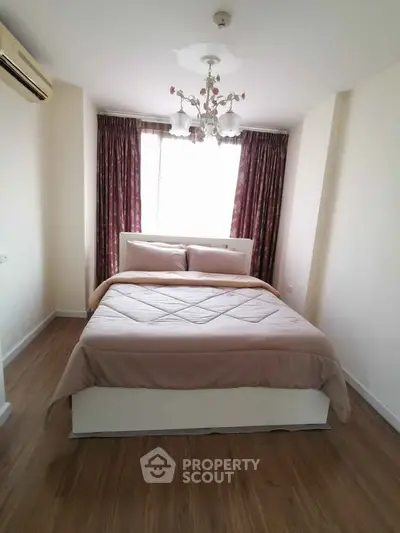 Cozy bedroom with elegant chandelier and large window, featuring stylish curtains and wooden flooring.