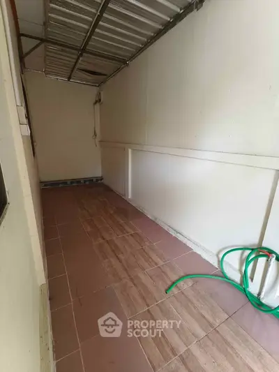 Narrow tiled corridor with metal roof and garden hose, ideal for storage or utility use.