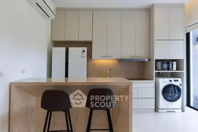 Modern kitchen with sleek cabinetry, island seating, and built-in appliances including a washing machine.