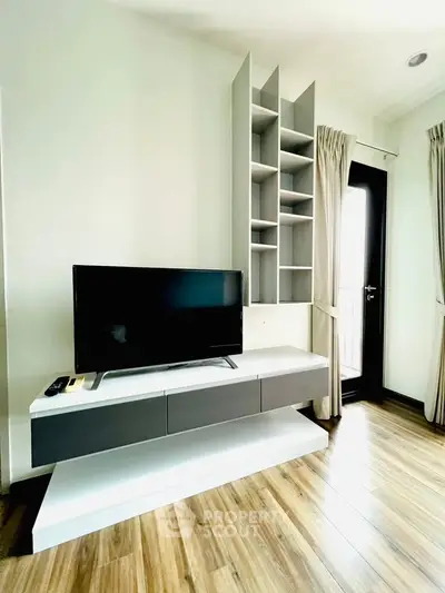 Modern living room with sleek TV stand and wooden flooring, featuring a stylish shelving unit and balcony access.