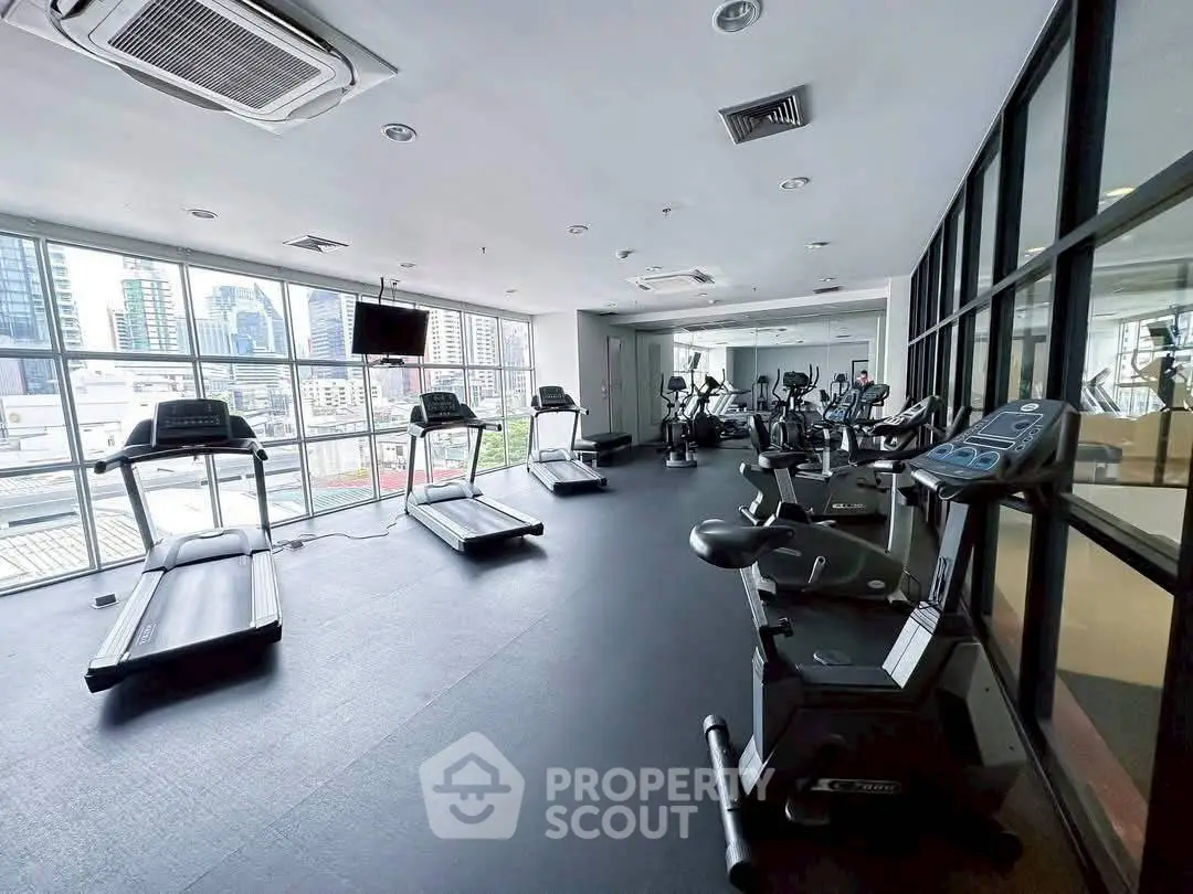 Spacious gym with modern equipment and city view, perfect for fitness enthusiasts.