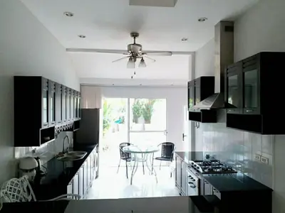 Modern kitchen with sleek black countertops and open layout leading to a bright dining area with garden view.