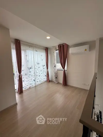 Spacious living room with wooden flooring and large windows featuring butterfly curtains, perfect for natural light.