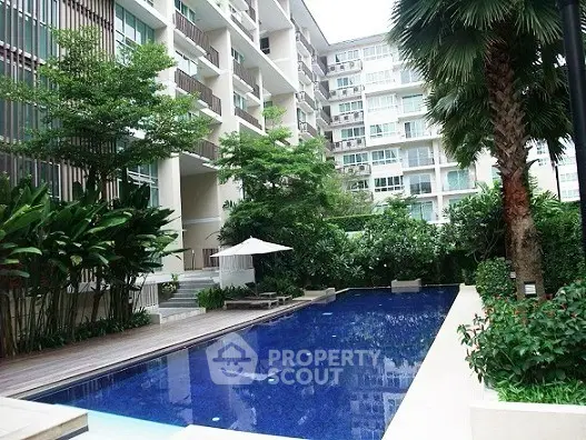 Luxurious condominium with a stunning pool surrounded by lush greenery and modern architecture.