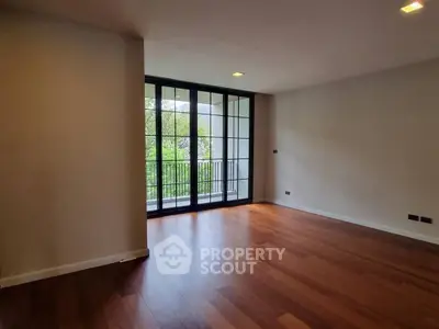Spacious living room with hardwood floors and large windows opening to a balcony.