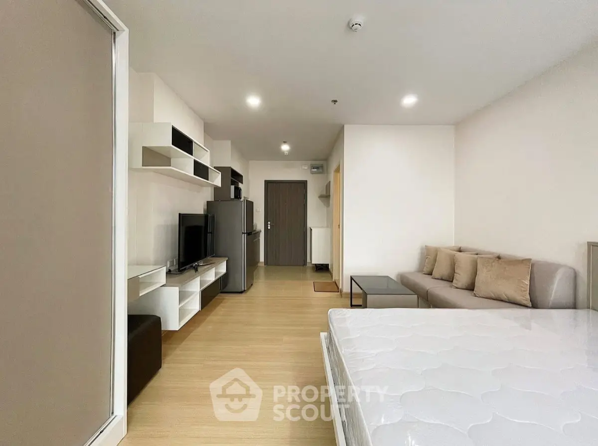 Modern studio apartment with open layout, featuring a cozy living area and sleek kitchen appliances.
