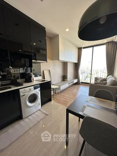 Modern living room with sleek kitchen and washing machine, featuring large windows and stylish decor.