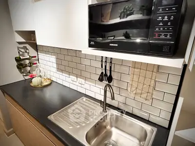Modern kitchen with sleek black countertop, stainless steel sink, and microwave, featuring stylish subway tile backsplash.