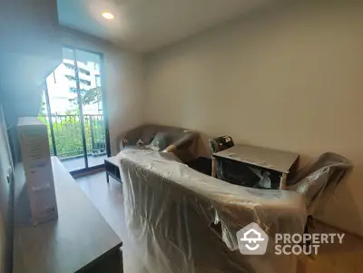 Modern living room with balcony view, featuring new furniture covered in protective plastic.