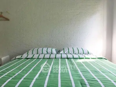 Cozy bedroom with green striped bedding and white brick wall, perfect for relaxation.