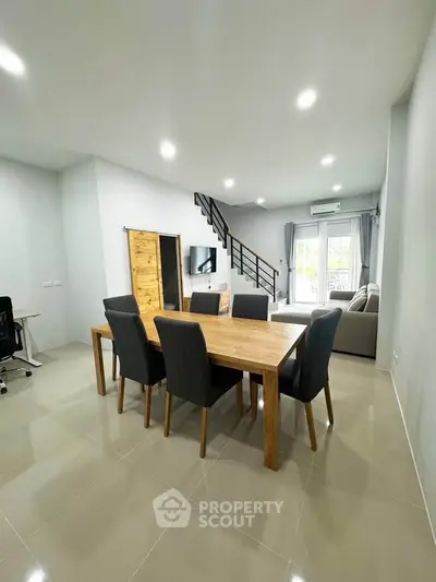 Spacious modern living room with dining area and staircase, featuring sleek furniture and ample natural light.