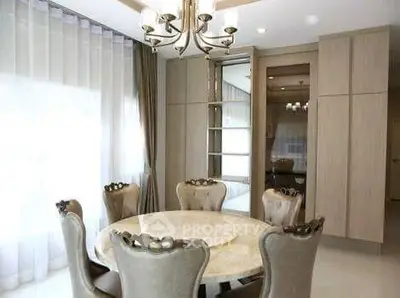 Elegant dining room with round marble table and plush chairs, featuring modern chandelier and floor-to-ceiling windows.