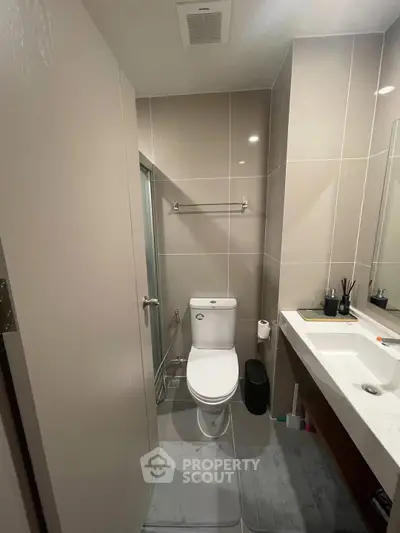 Modern bathroom with sleek fixtures and neutral tiles, featuring a toilet and a stylish sink area.