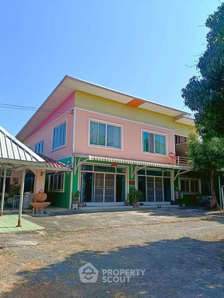 Charming two-story colorful house with spacious driveway and lush greenery, perfect for family living.