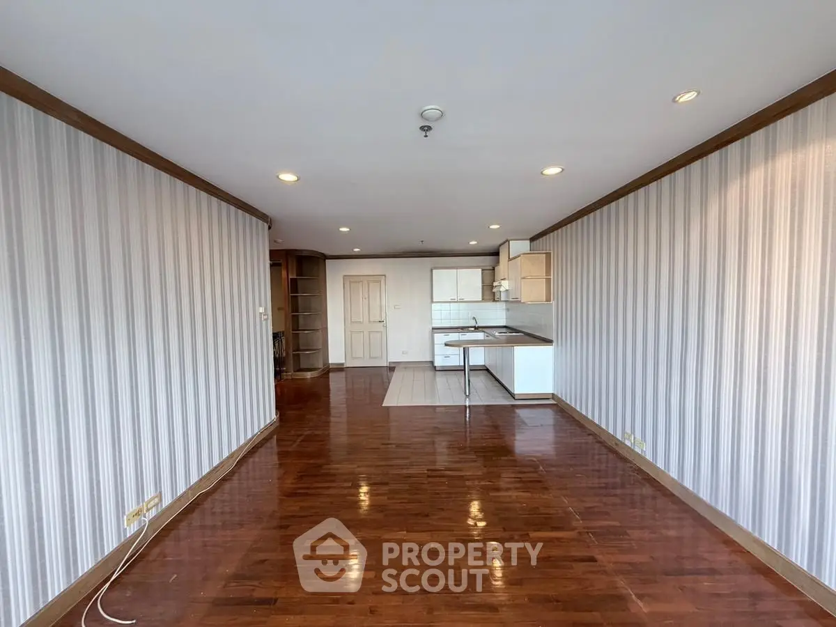 Spacious open-plan living room with wooden flooring and modern kitchen area.