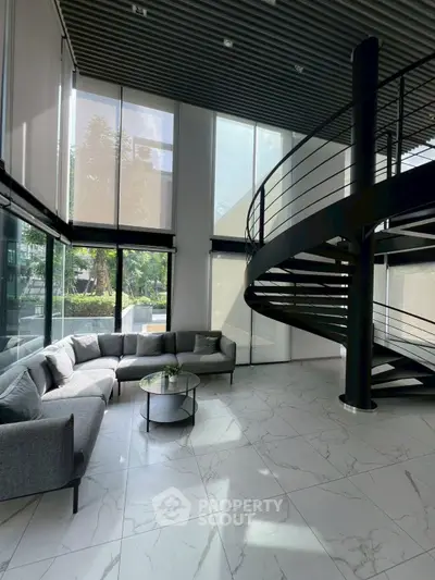Modern living room with spiral staircase and large windows, featuring sleek gray furniture and marble flooring.