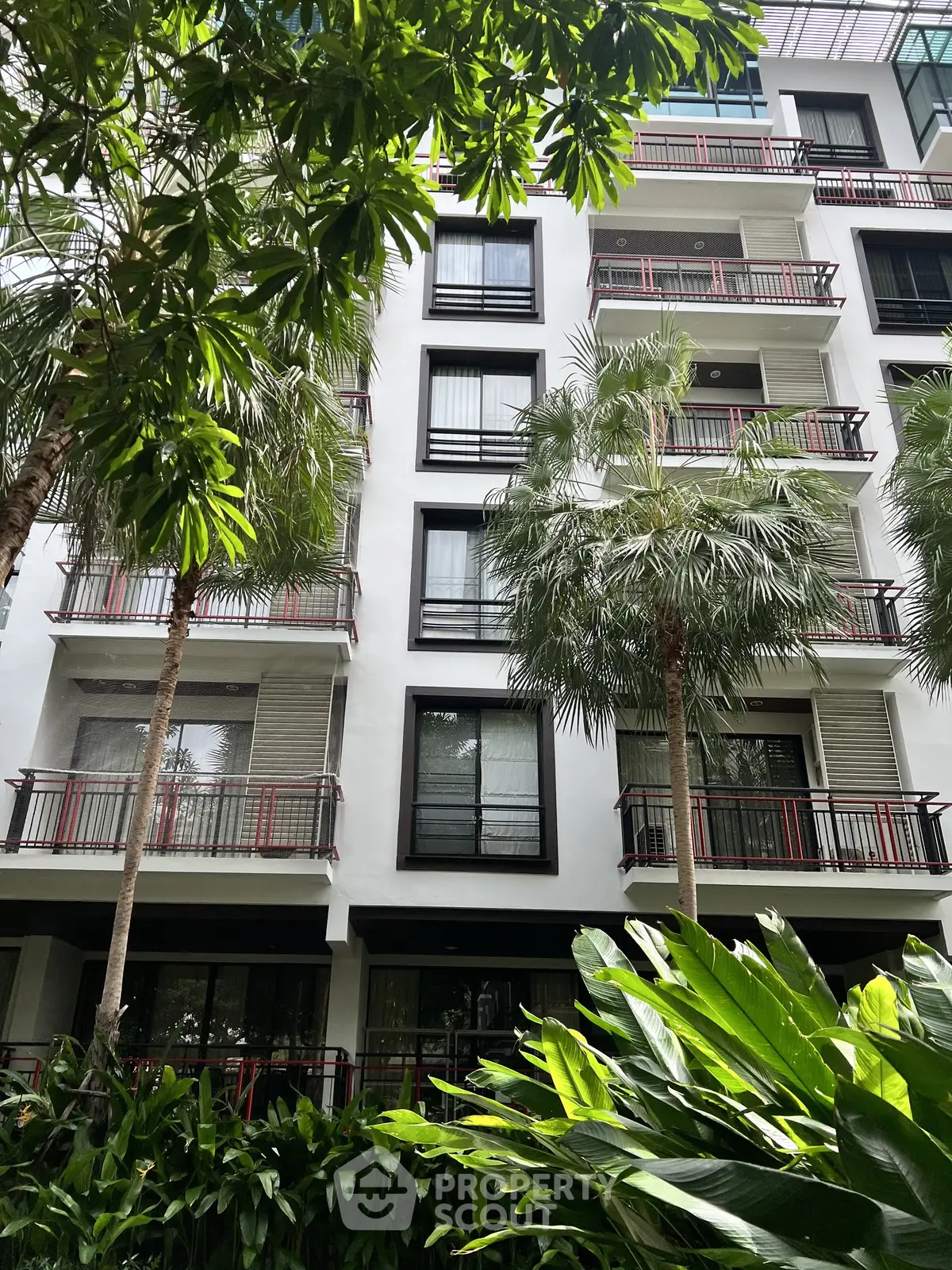 Modern apartment building with lush greenery and balconies in urban setting.