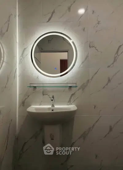 Modern bathroom with marble walls and illuminated round mirror above a sleek sink.