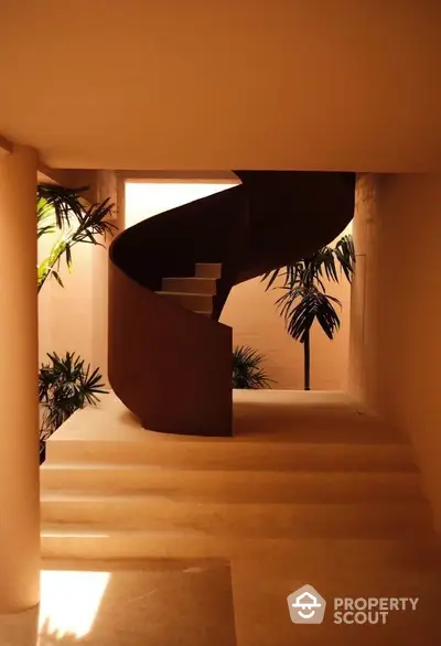 Elegant spiral staircase in modern architectural interior with warm lighting and lush greenery