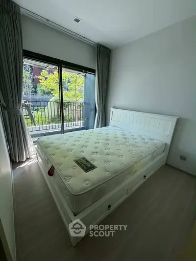 Bright bedroom with large window and garden view, featuring a white bed frame and light wood flooring.