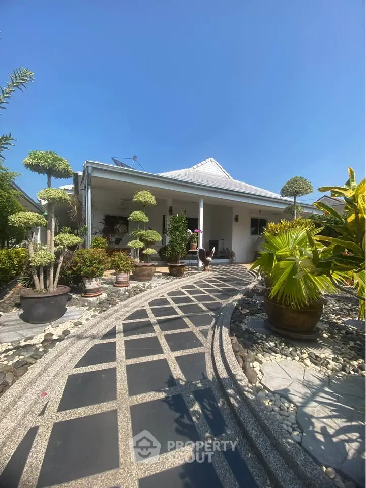 Charming house with landscaped garden and inviting entrance path under clear blue sky.