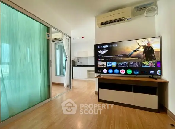 Modern living room with large TV and air conditioning, open layout to kitchen, wooden flooring.